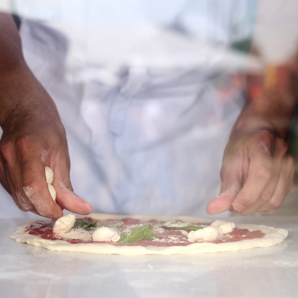 Chef's hands making fresh pizza with cheese and sauce.